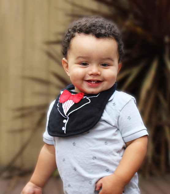 Child wearing a gray outfit with a black bib and red bow tie, standing outdoors.