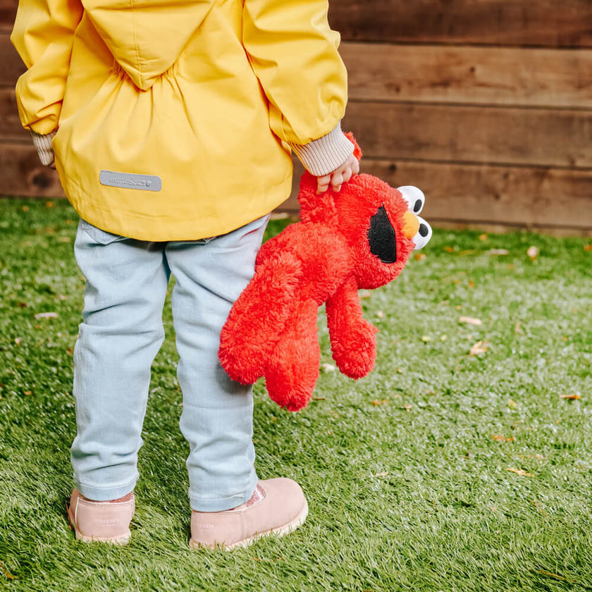 Child holding a colorful soft Elmo toy in the garden