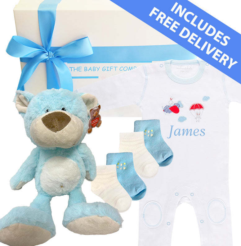Baby gift set with blue teddy bear, white romper, and socks from The Baby Gift Company.