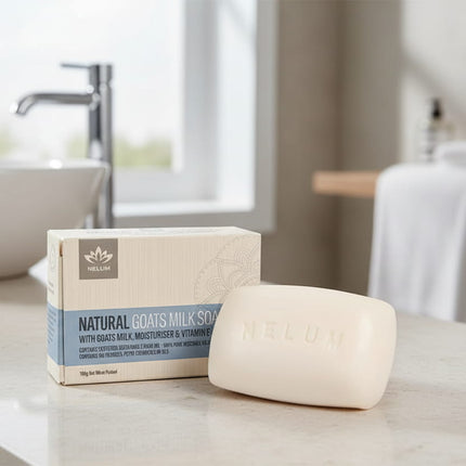 Bar of soap and box with 'NELUM' branding , with a sink and towel in background on a tiled surface.
