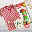 Red and white striped baby onesie with hungry caterpillar toys and a snack box on a wooden surface