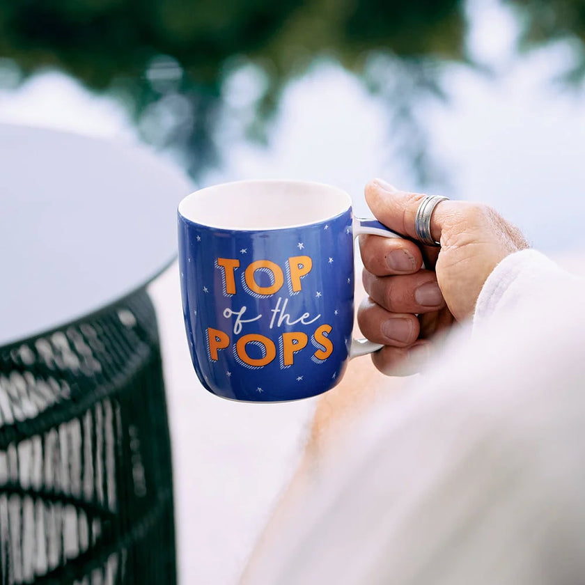 Hand holding a blue mug with 'Top of the Pops' text outdoors