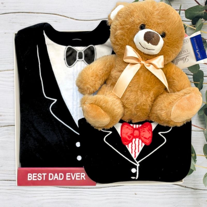 Teddy bear in a black tuxedo with a 'Best Dad Ever' sign on a wooden surface.