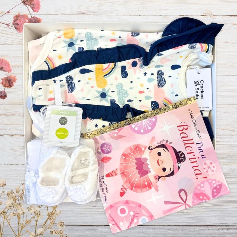 Baby gift hamper with shoes, blanket, and book on a wooden surface