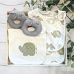 Set of baby bibs and toys with elephant patterns in a gift box on a wooden surface.