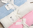 Three baby blankets in blue, white, and pink with 'ES Kids' tags on a wooden surface.