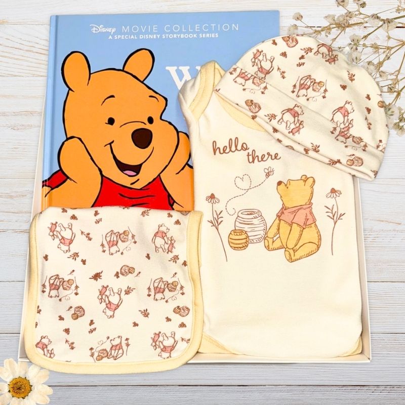 Winnie the Pooh-themed children's clothing and book on a wooden surface.