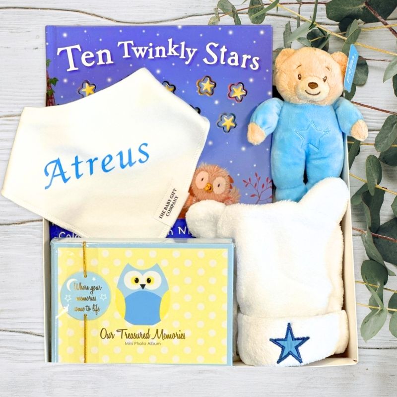 Baby gift set with teddy bear, book, and photo album on a wooden surface.