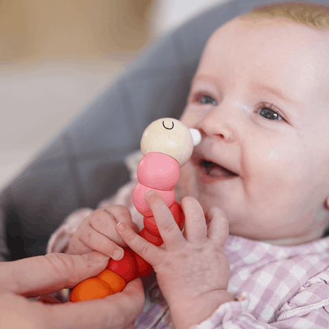 Baby holding red wooden Worm toys