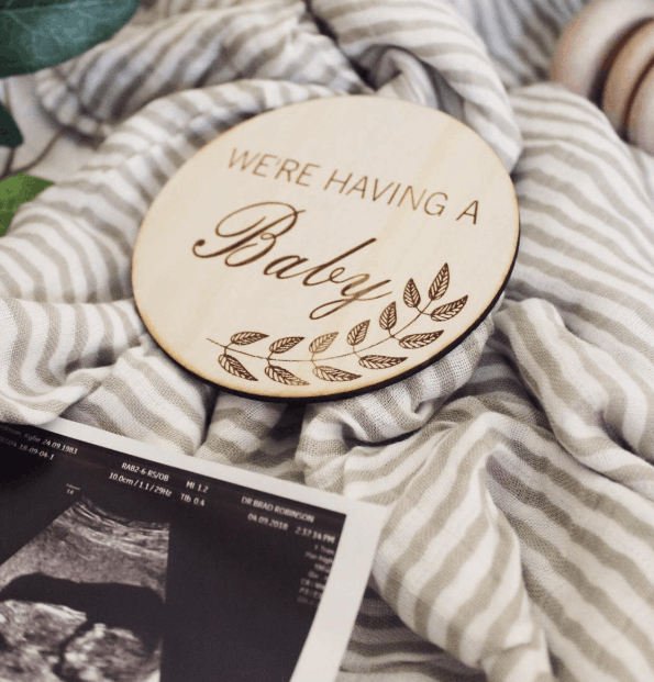 Wooden disc with 'We're Having a Baby' text on a striped fabric background