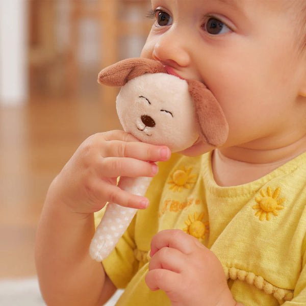 Baby in a yellow outfit holding a dog-shaped rattle