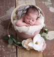 Newborn baby sleeping in a pink bucket with flowers on a wooden floor.