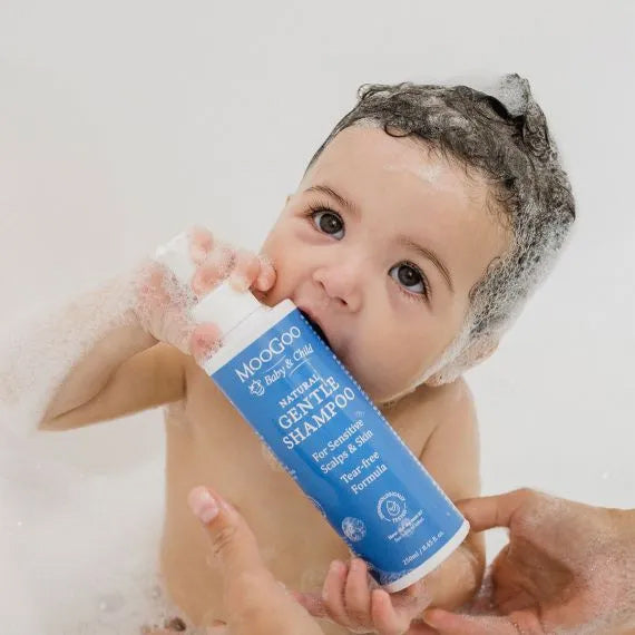 Baby holding a bottle of MooGoo baby shampoo with soapy hair.