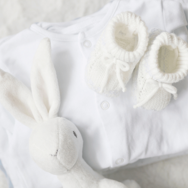 White baby outfit with booties and a soft toy on a light background