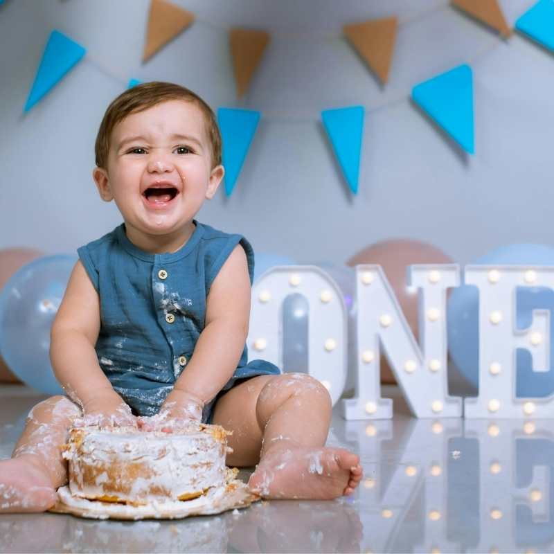 Child celebrating a first birthday with a cake, surrounded by decorative letters spelling 'ONE' and colorful flags.