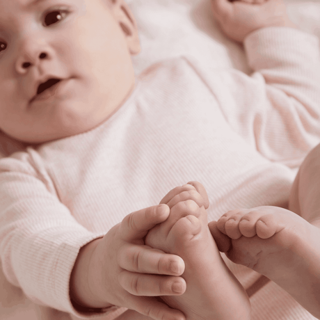 Baby in a pink outfit holding its feet