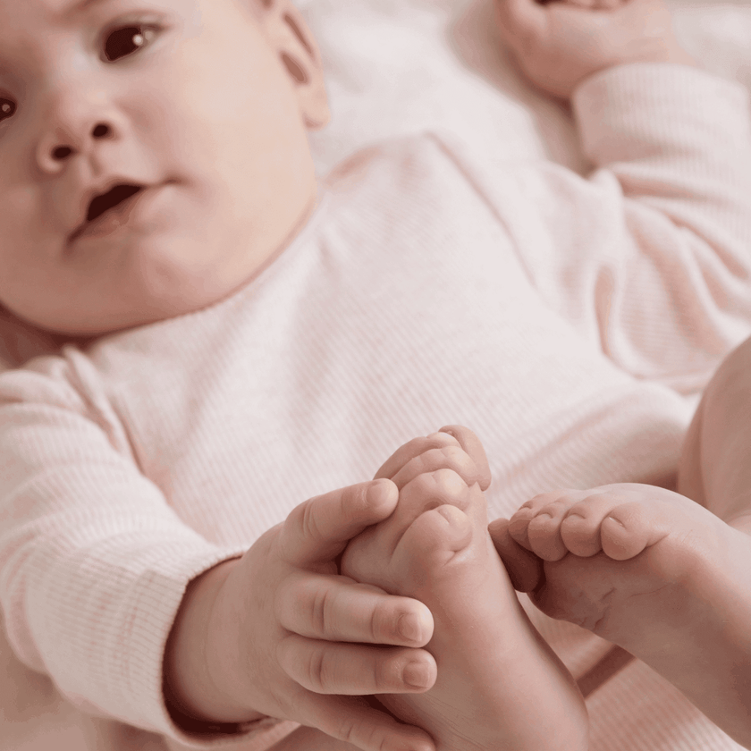 Baby in a pink outfit holding its feet