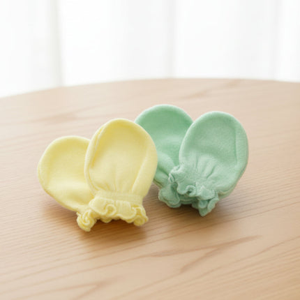 Two small baby mittens, yellow and green items on a wooden table background.