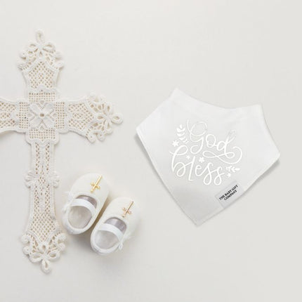 White cross, baby shoes, and bib with 'God bless' text on a light gray background