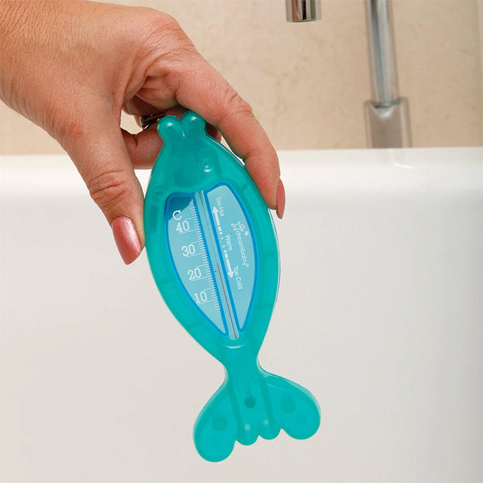 Hand holding a fish-shaped water temperature tester over a bathtub.
