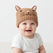 Baby wearing brown knitted cat hat with pink ears on a light background
