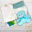 Blue teddy bear with a bow tie , baby clothes in a gift box on a surface