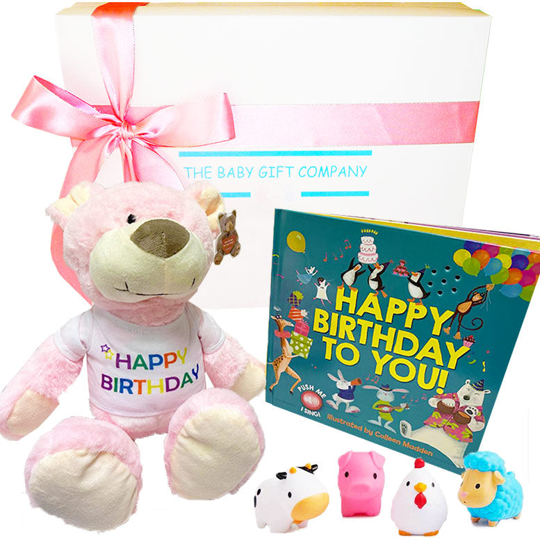 Pink teddy bear with 'Happy Birthday' shirt, colorful book, and small toys on a white background.