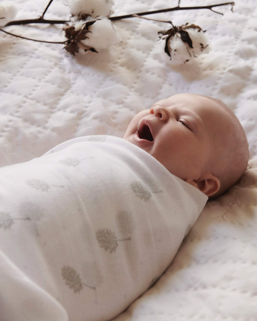 Baby wrapped in a white blanket with gray patterns, lying on a textured white surface.