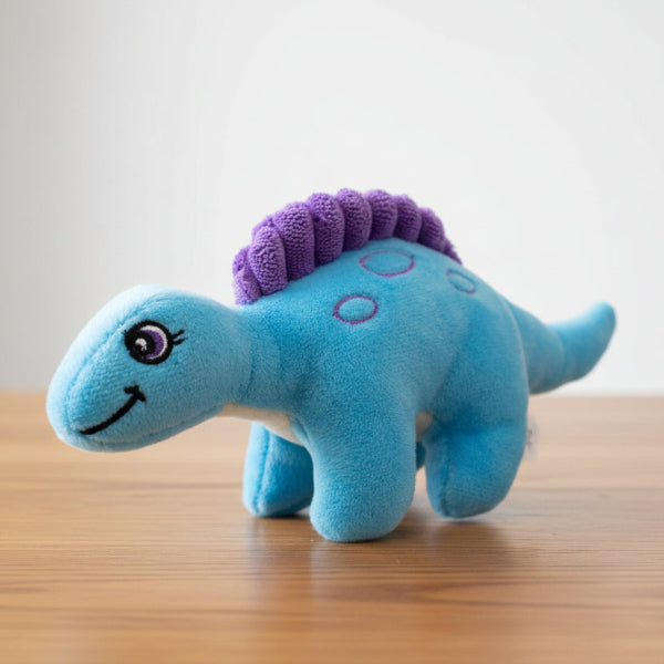 Blue plush dinosaur toy with a purple spiky back on a table