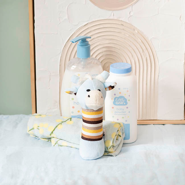 Baby products including a plush toy, bottles, and a blanket on a white surface with a neutral-colored wall in the background.