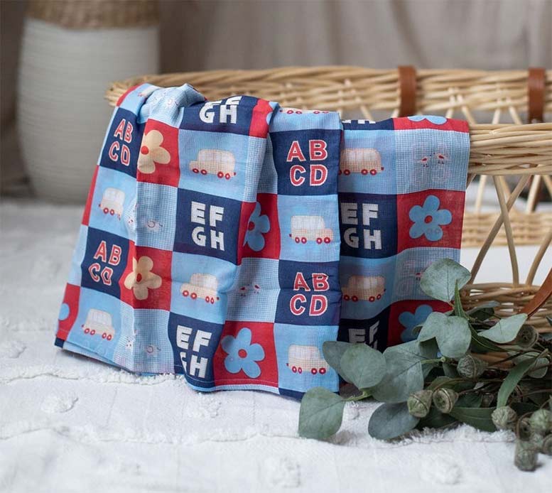 Three colorful baby blankets with alphabet and vehicle patterns draped over a wicker basket.