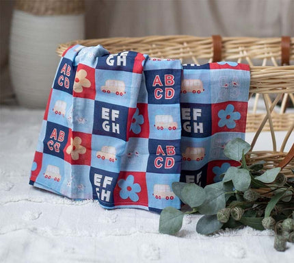 Three colorful baby blankets with alphabet and vehicle patterns draped over a wicker basket.