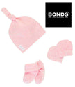 Pink baby hat, socks, and mittens set with Bonds logo on a white background