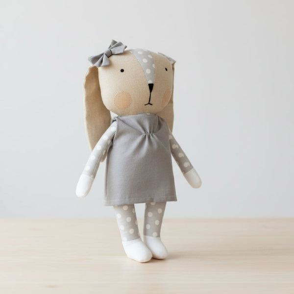 Stuffed toy rabbit with a gray dress and bow on table