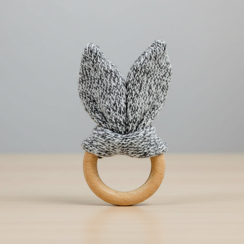 Teething ring with knitted bunny ears and wooden base on a table background