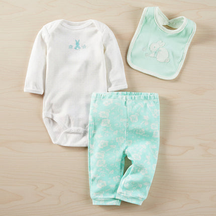 Baby clothing set with white long-sleeve bodysuit, green pants, and bib on a wooden background