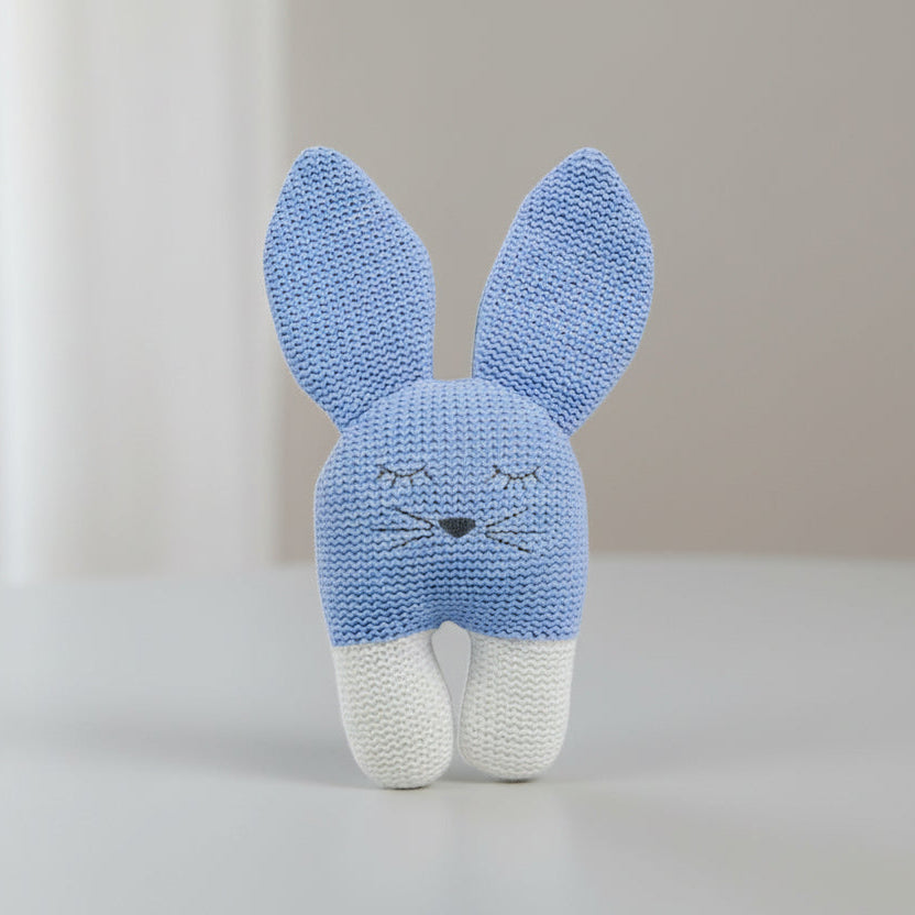 Knitted blue bunny toy with white feet on a table background