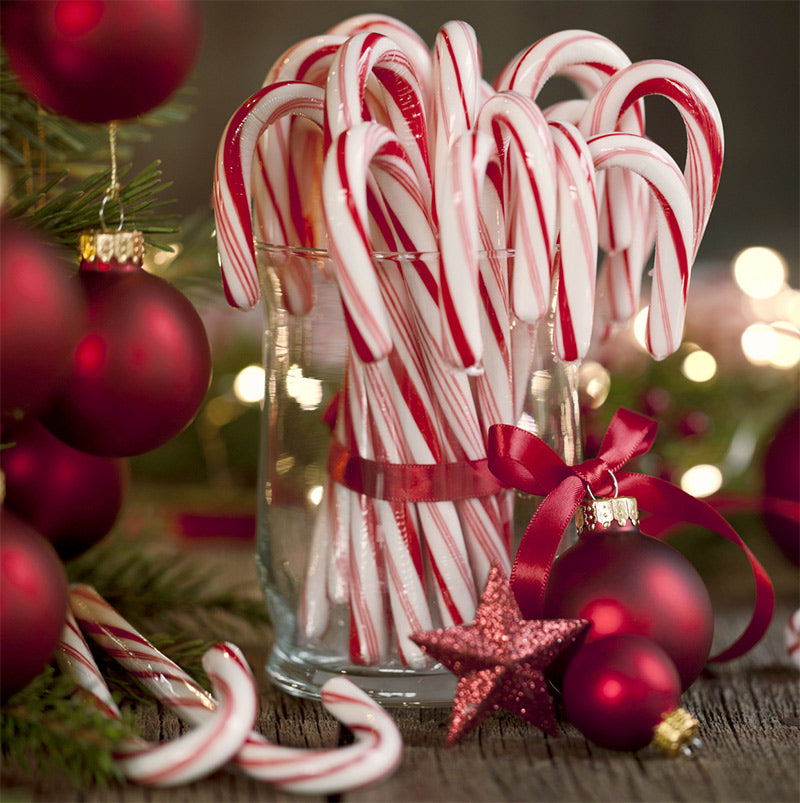 Glass jar filled with candy canes surrounded by Christmas ornaments on a wooden surface.
