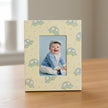 Baby photo frame with a baby picture inside, featuring a baby in a blue outfit and white hat against a light blue background.