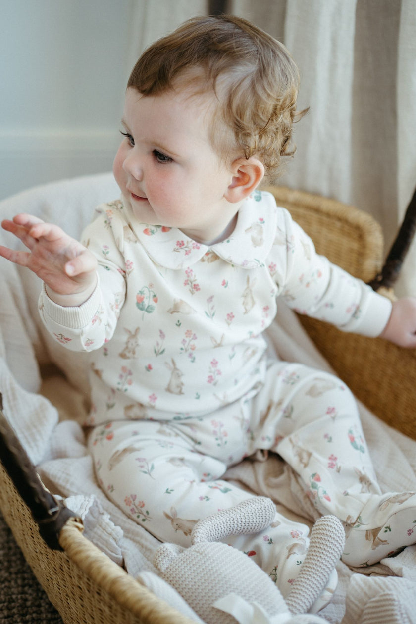 Baby in a floral outfit sitting in a wicker chair.