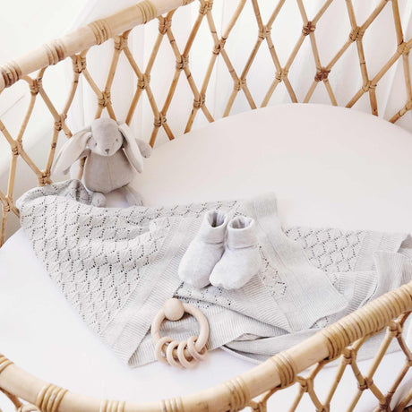 Wicker crib with baby items including a blanket, shoes, and toys in a bright room.