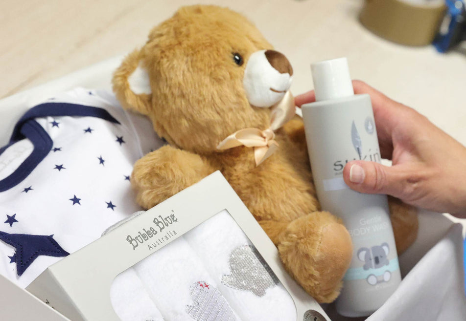 Teddy bear, baby clothes, and other baby gifts in a box