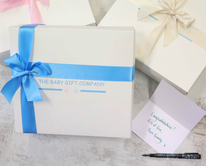 Gift box with blue ribbon and card on a textured surface, featuring 'The Baby Gift Company'.