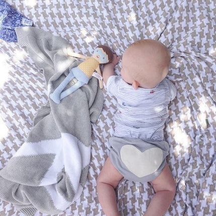 Baby lying on a patterned blanket with a gray blanket and toy nearby