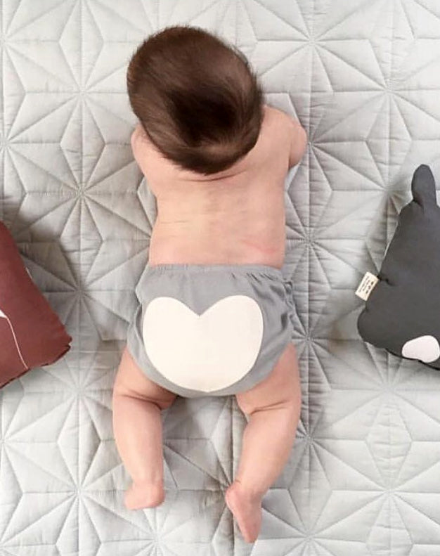 Baby wearing a heart-patterned diaper on a quilted surface