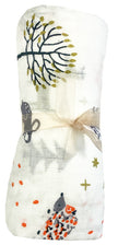 Baby blanket with nature-themed design featuring trees and animals, wrapped in a clear plastic bag.