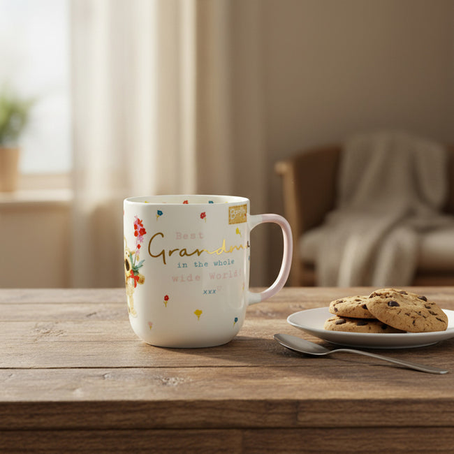 White mug featuring a floral design and the word 'Best Grandma', on a wooden surface with cookies and a spoon.