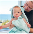 Baby wrapped in a light green towel with ears, held by an adult outdoors.