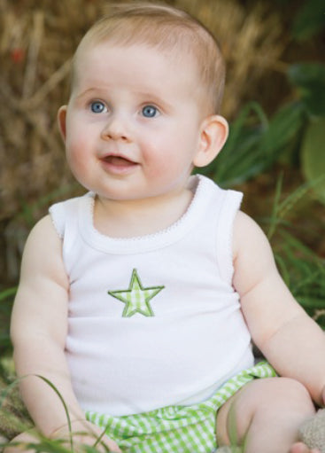 Baby wearing a white sleeveless shirt with a green star and green checkered shorts sitting outdoors.
