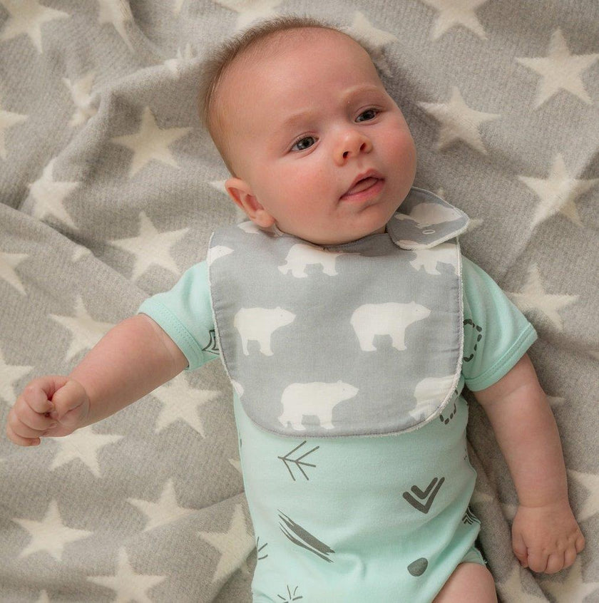 Baby wearing a light blue onesie with bear pattern and gray bib on a star-patterned blanket